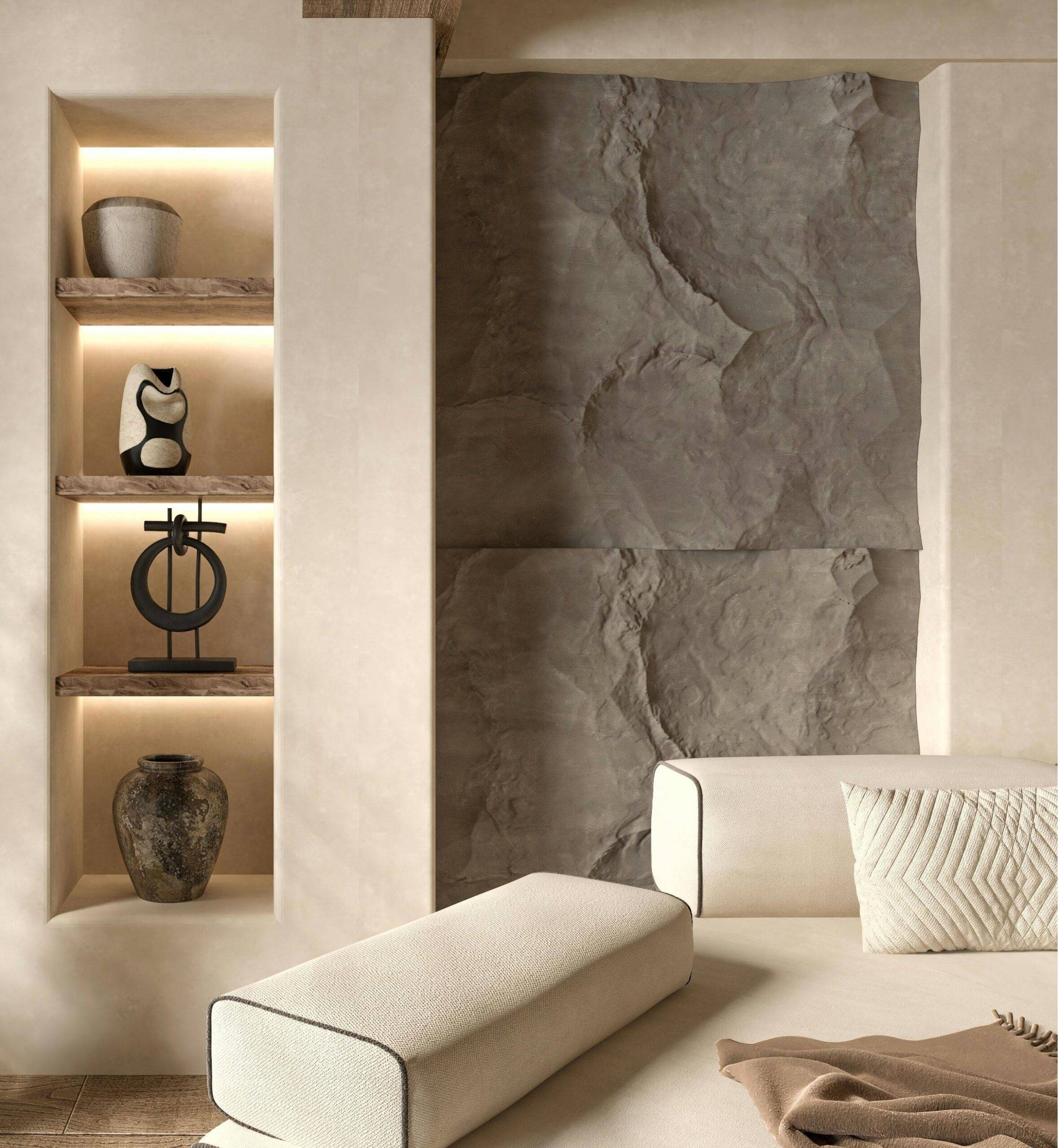 Un salon minimaliste avec un canapé beige clair doté d'un coussin de dossier matelassé. À gauche, une étagère encastrée à trois niveaux présente un vase, une sculpture abstraite et un autre vase. Le mur présente des panneaux de pierre texturés, complétant les tons neutres de la pièce.