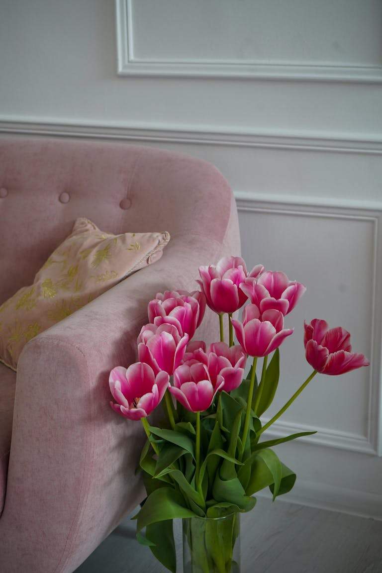 A beautiful arrangement of pink tulips beside an elegant pink sofa, creating a serene indoor ambiance.